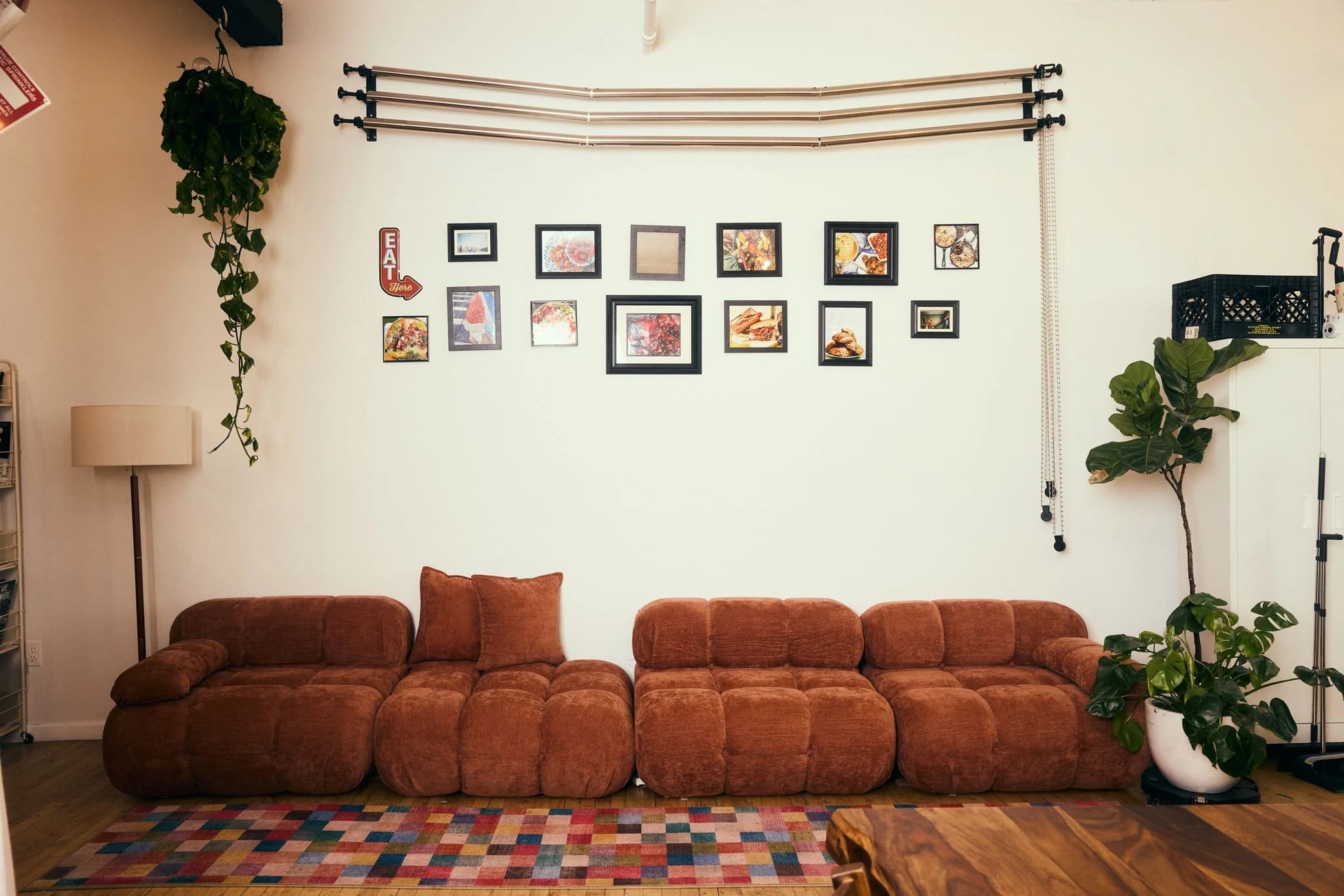The lounge with a rust-colored sofa, framed food photography, and a colorful rug
